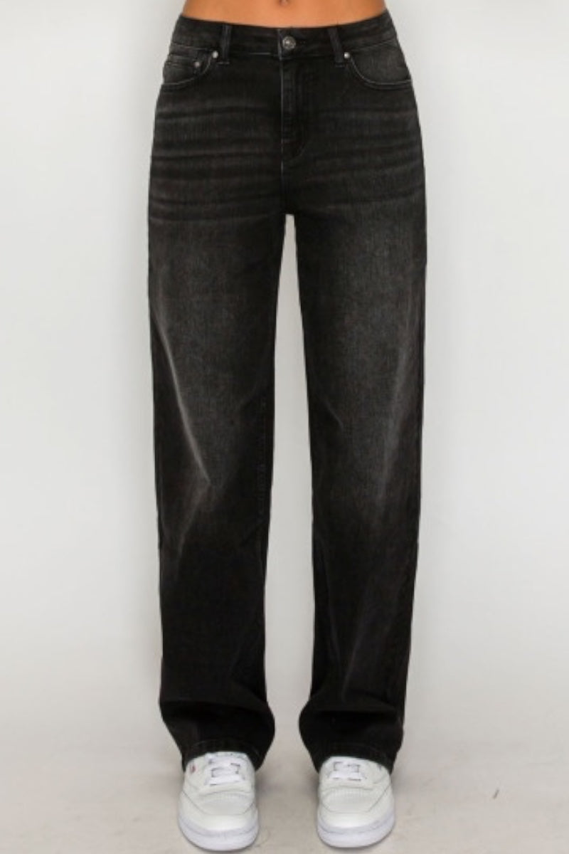 A person wearing black high-waisted, wide-leg denim jeans with white sneakers, shown from the waist down against a plain light background.