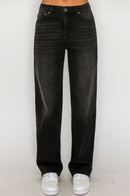 A person wearing black high-waisted, wide-leg denim jeans with white sneakers, shown from the waist down against a plain light background.