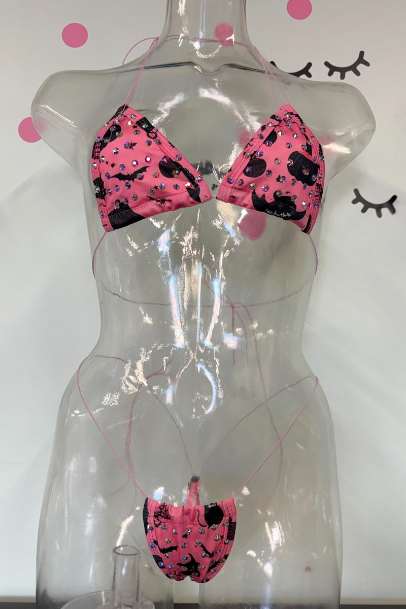 Pink and black cat-patterned bikini set displayed on a transparent mannequin torso against a white wall with polka dots.
