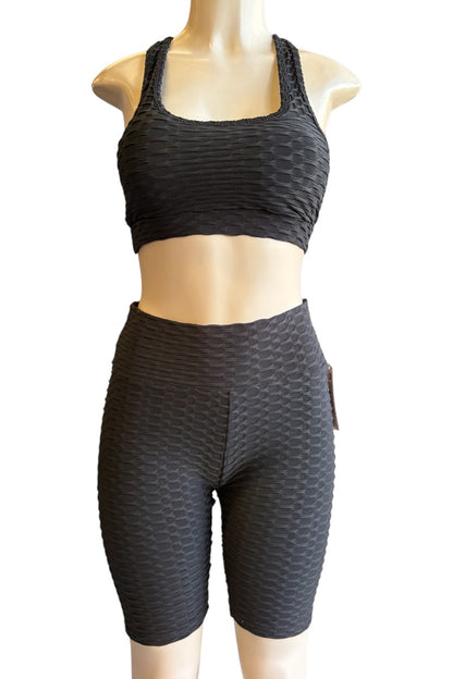 A two-piece activewear set consisting of a black textured sports bra and matching high-waisted biker shorts, displayed on a beige mannequin torso against a plain white background.