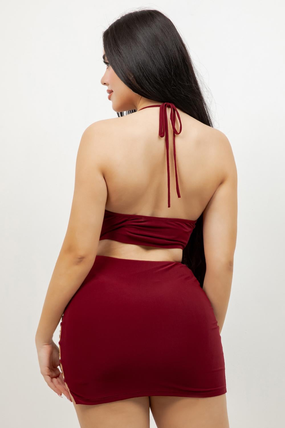 A woman shown from the back wearing a deep burgundy two-piece dress consisting of a halter crop top and a matching high-waisted mini skirt, against a plain white studio background.