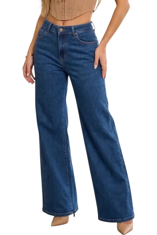 A model wearing a pair of high-waisted, wide-leg blue denim jeans with a straight-to-flared leg, paired with a beige crop top and beige heels, shown against a plain white background.