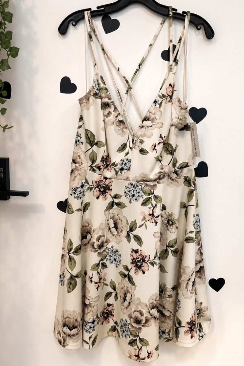 A sleeveless floral print dress with thin criss-cross straps, hanging on a black hanger against a white wall decorated with black heart cutouts.