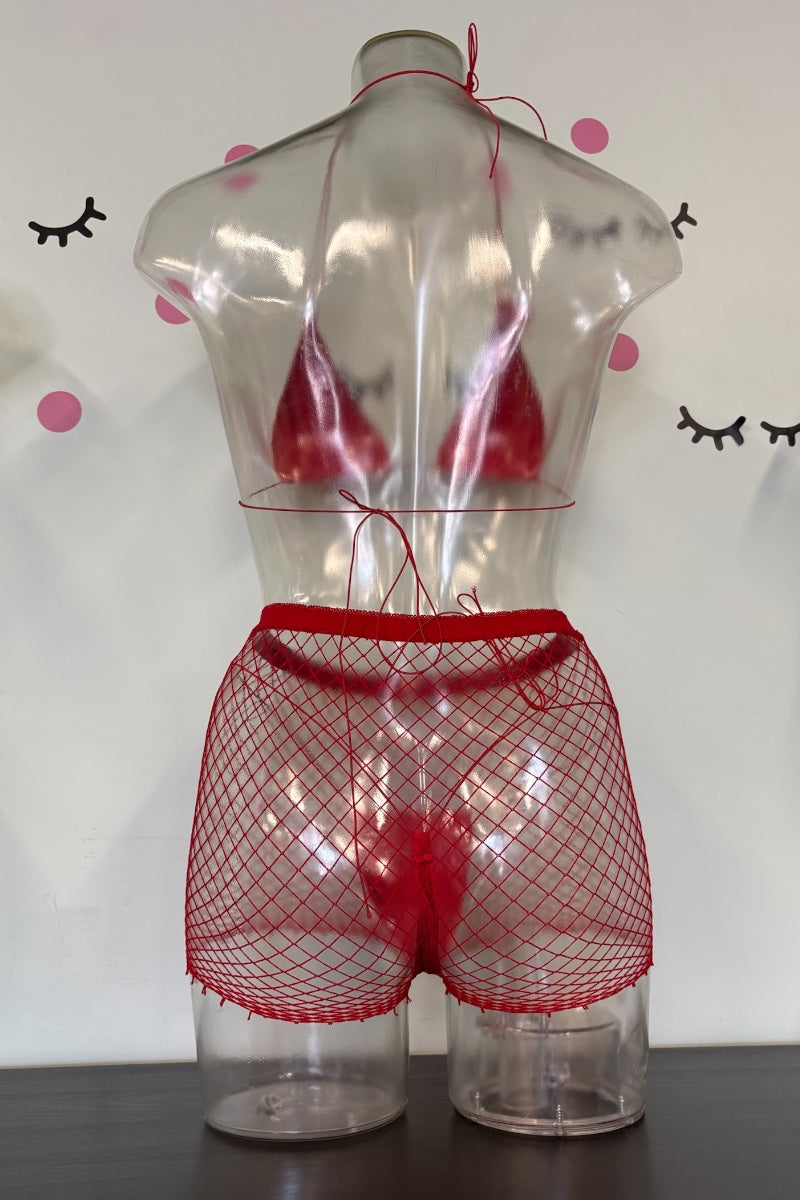 Red fishnet lingerie set consisting of a bikini top and matching shorts, displayed on a clear plastic torso mannequin against a white wall with decorative eyelashes and pink dots.