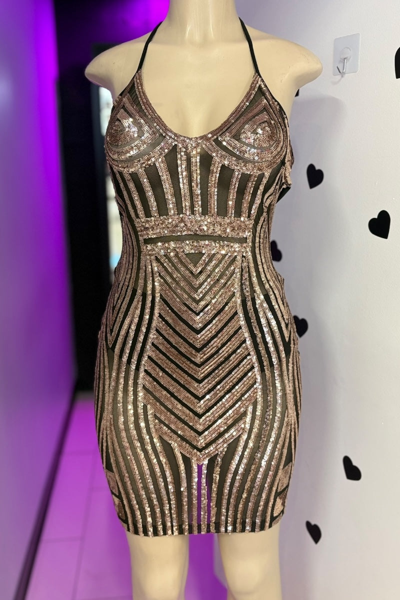 Gold sequin dress on a mannequin against a white wall with black hearts.