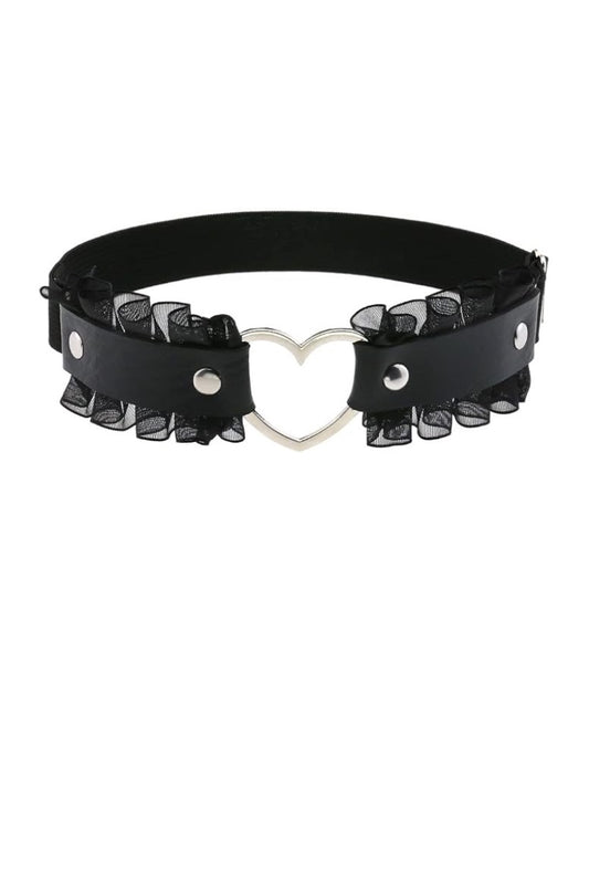 A black faux-leather leg garter featuring a central silver heart-shaped metal clasp and layered black sheer ruffled trim on both sides, displayed against a solid white background.