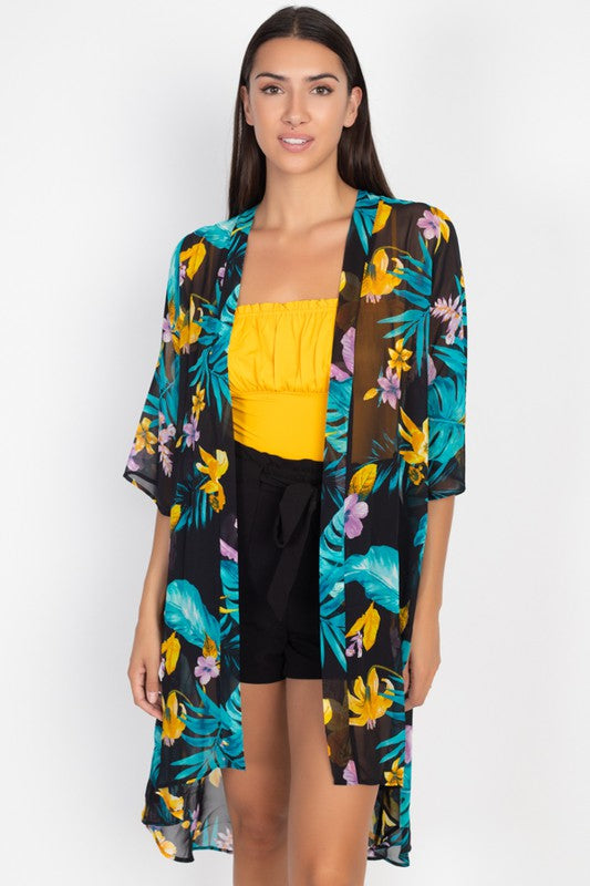 Woman wearing a floral kimono over a yellow top and black shorts on a white background