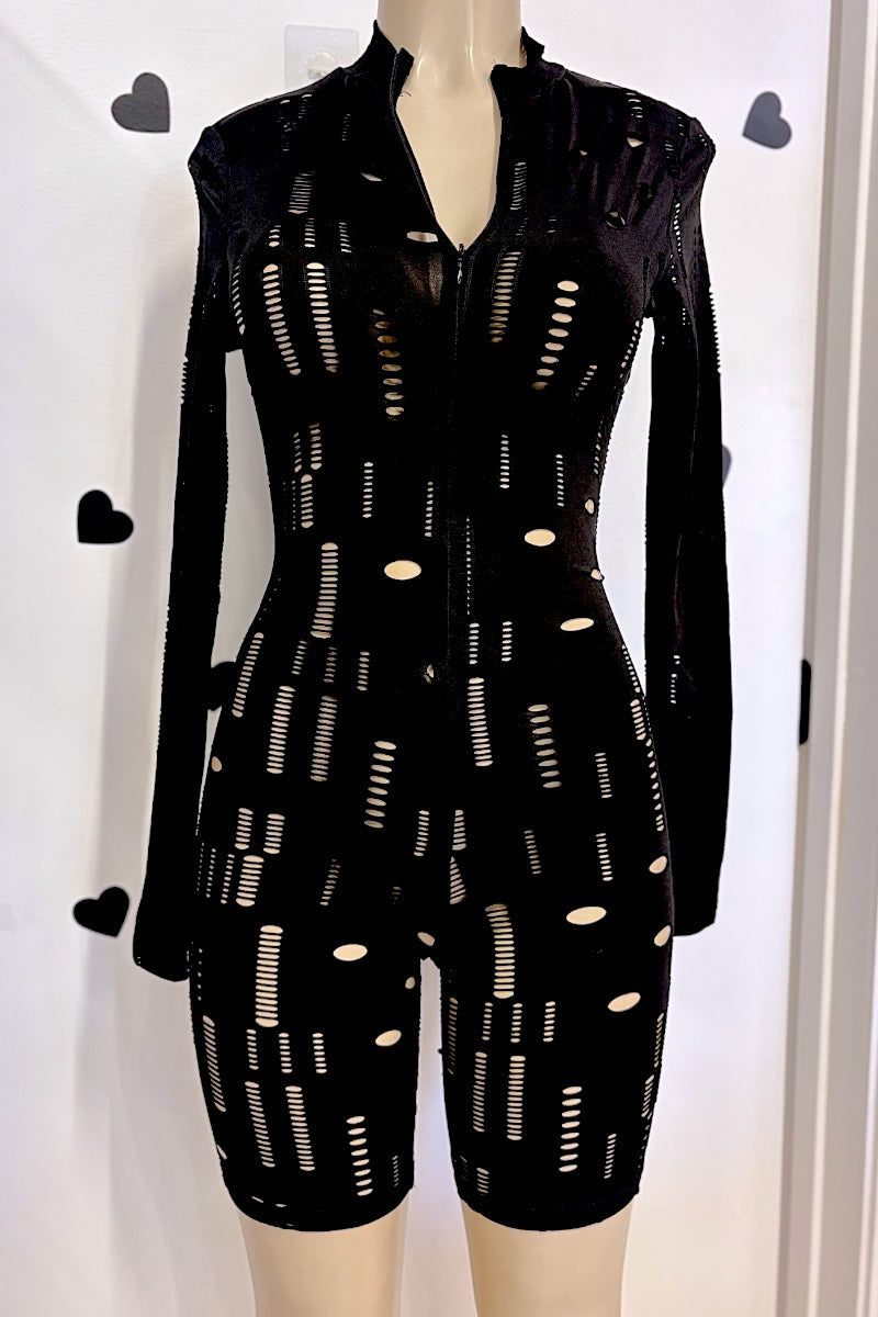 A black long-sleeve romper with a front zipper and cutout pattern, displayed on a mannequin against a white wall with heart-shaped decorations.