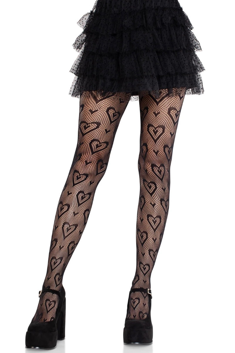 Black tights with a repeating heart pattern, worn by a model with a black ruffled mini skirt and black platform heels against a white background.