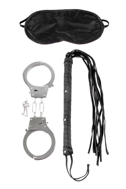 Set of black leather flogger, silver handcuffs, and black satin eye mask on a white background