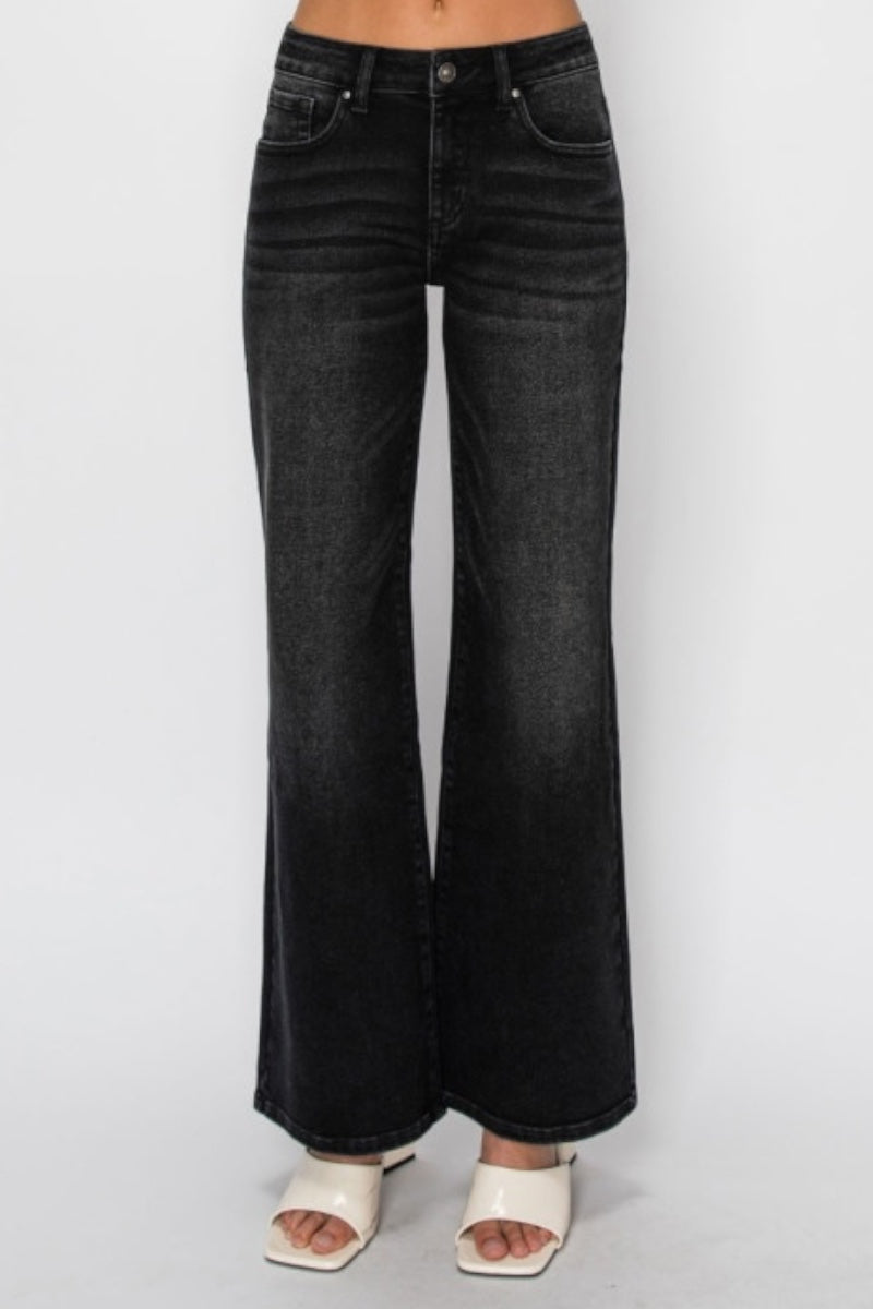 A person wearing black wide-leg denim jeans with a faded wash, paired with white slide sandals, shown against a plain light gray studio background.