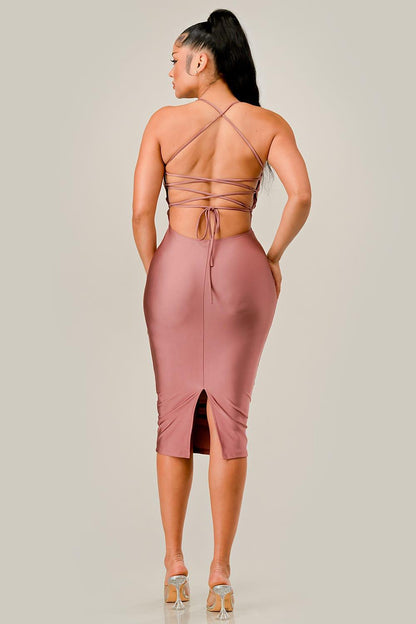 Woman wearing a pink dress with a strappy back design on a plain background