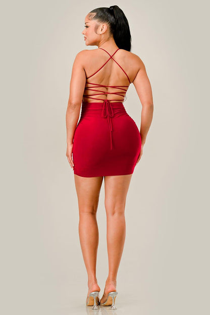 Woman wearing a red dress with criss-cross back design on a plain background