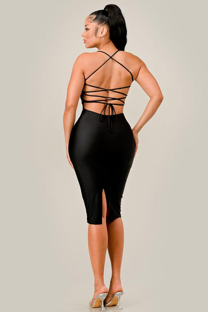 Woman wearing a black strappy dress with a slit on a plain background