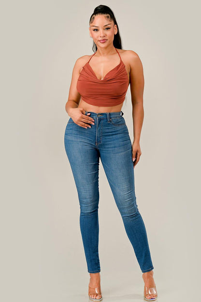 Woman wearing a rust-colored top and blue jeans on a plain background
