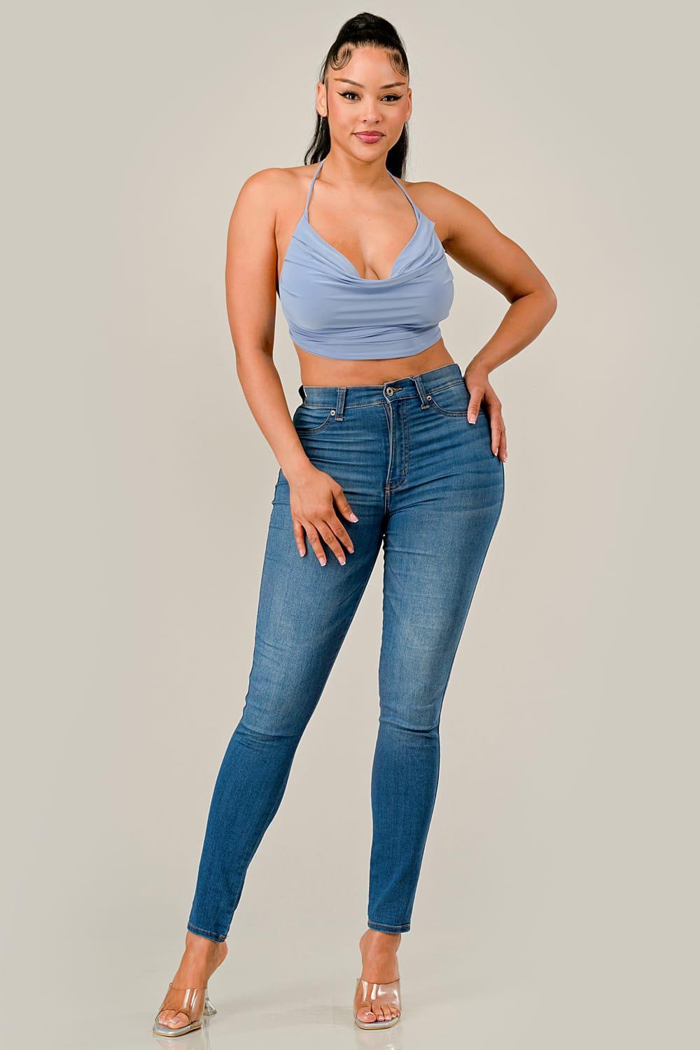 Woman wearing a light blue top and dark blue jeans on a plain background