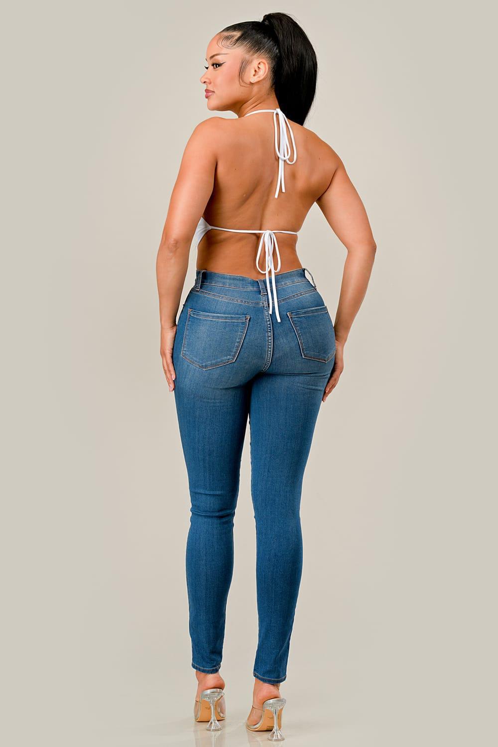 Woman wearing blue jeans and a white open-back top on a plain background
