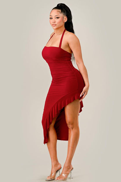 Woman wearing a red halter dress with an asymmetrical hem on a plain background
