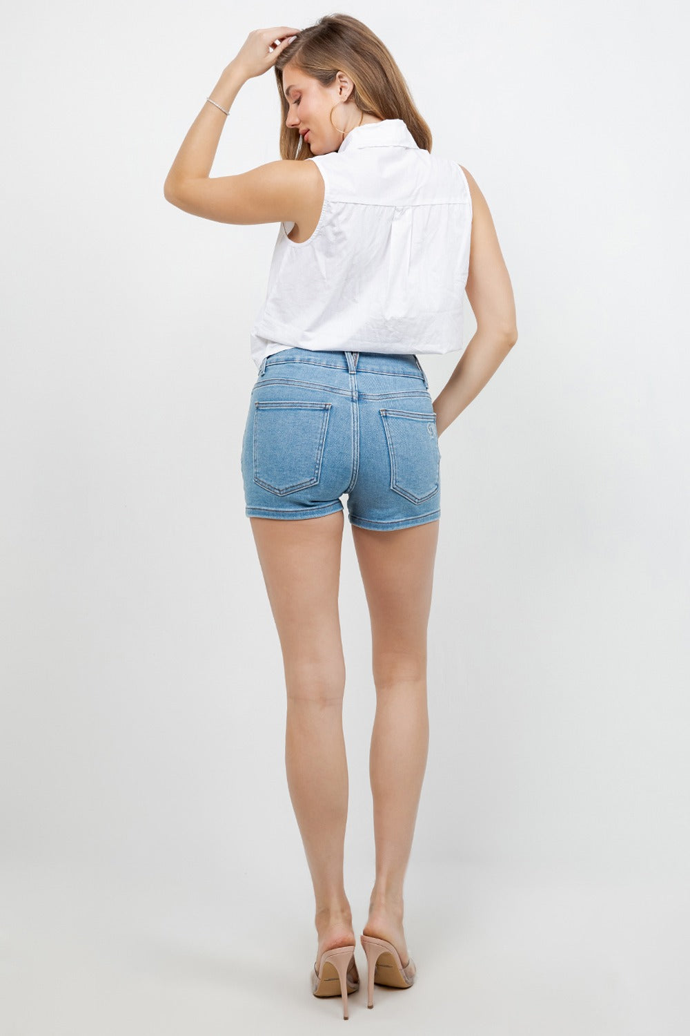 Woman wearing a white sleeveless top and blue denim shorts on a white background