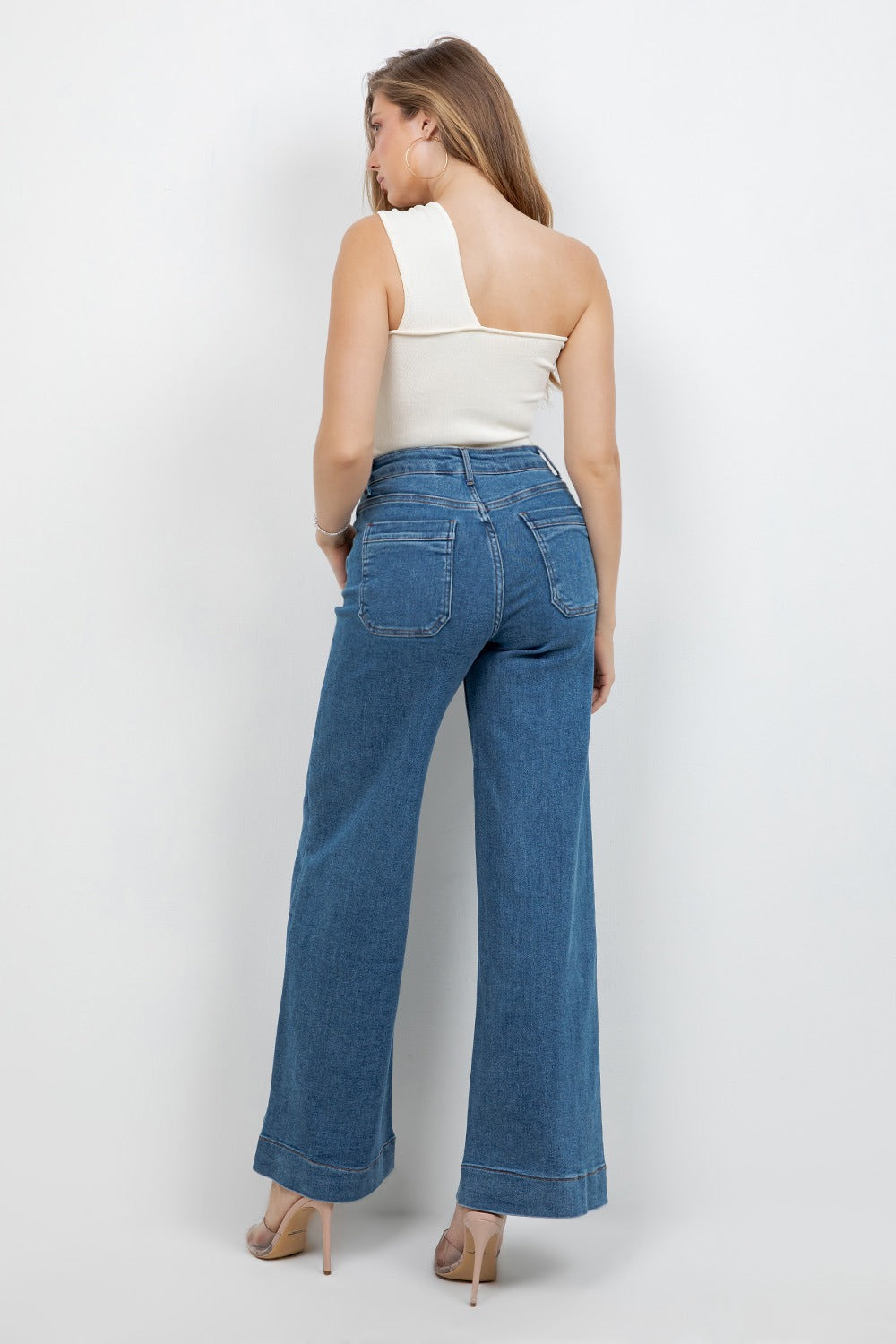 Woman wearing blue jeans and a white top on a plain background