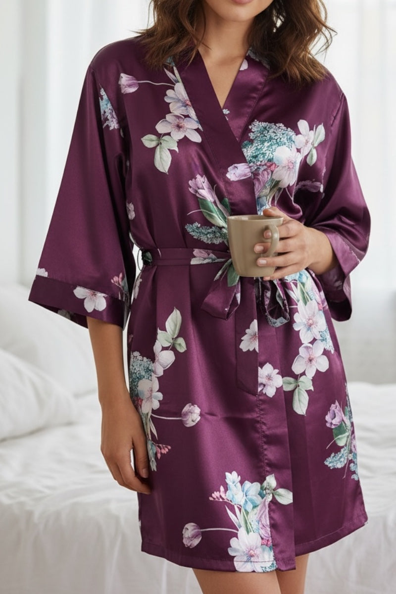Person wearing a purple floral satin robe holding a small bouquet of flowers.