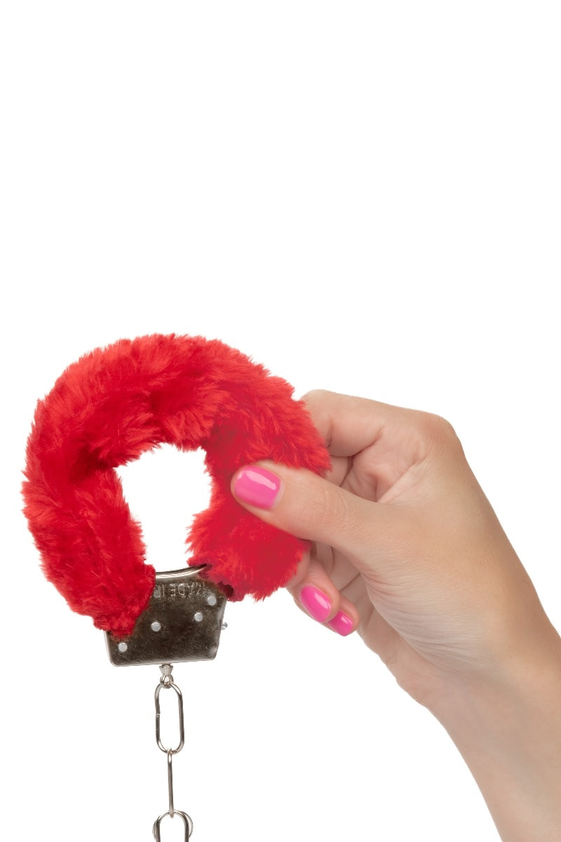 Red fluffy handcuff held by a hand with pink nail polish on a white background