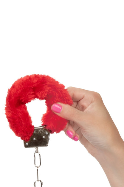 Red fluffy handcuff held by a hand with pink nail polish on a white background