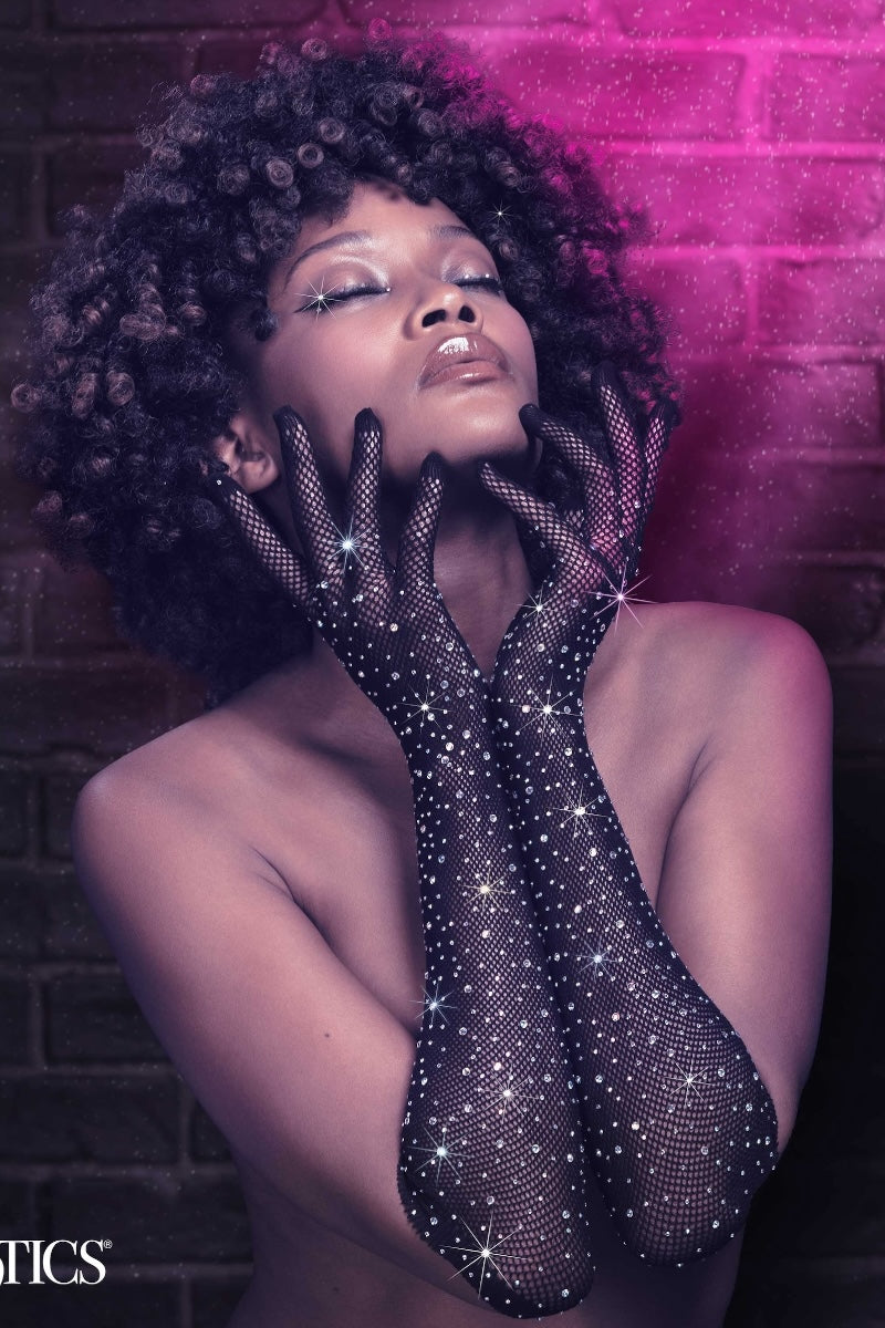 Woman wearing sparkling black gloves against a brick wall with pink lighting