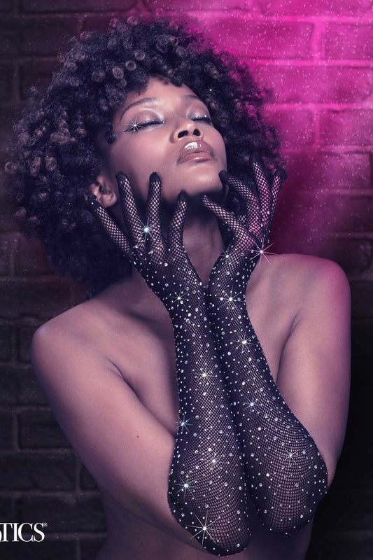 Woman wearing sparkling black gloves against a brick wall with pink lighting