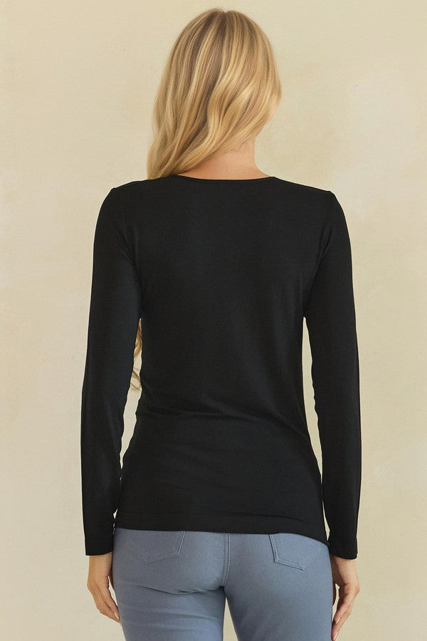 A woman viewed from the back wearing a black long-sleeve top and light blue pants against a plain beige background.