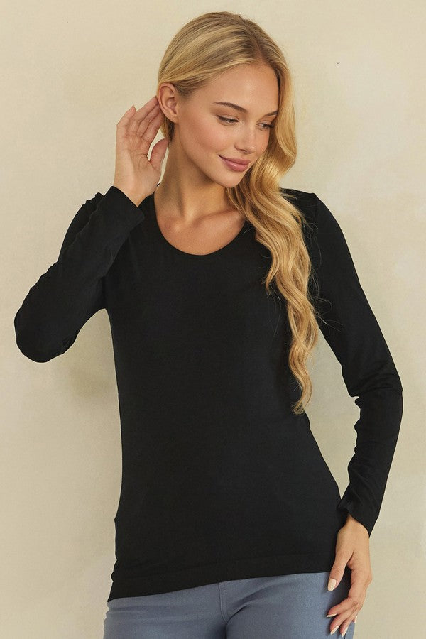 A blonde woman wearing a black long-sleeve crewneck top and gray pants, posing against a plain beige background.
