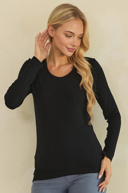 A blonde woman wearing a black long-sleeve crewneck top and gray pants, posing against a plain beige background.