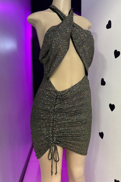 Mannequin wearing a sparkly black dress with a halter neck and open back against a purple and white background.