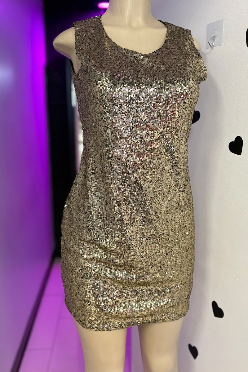 Gold sequin dress on a mannequin against a white wall with black heart shapes.