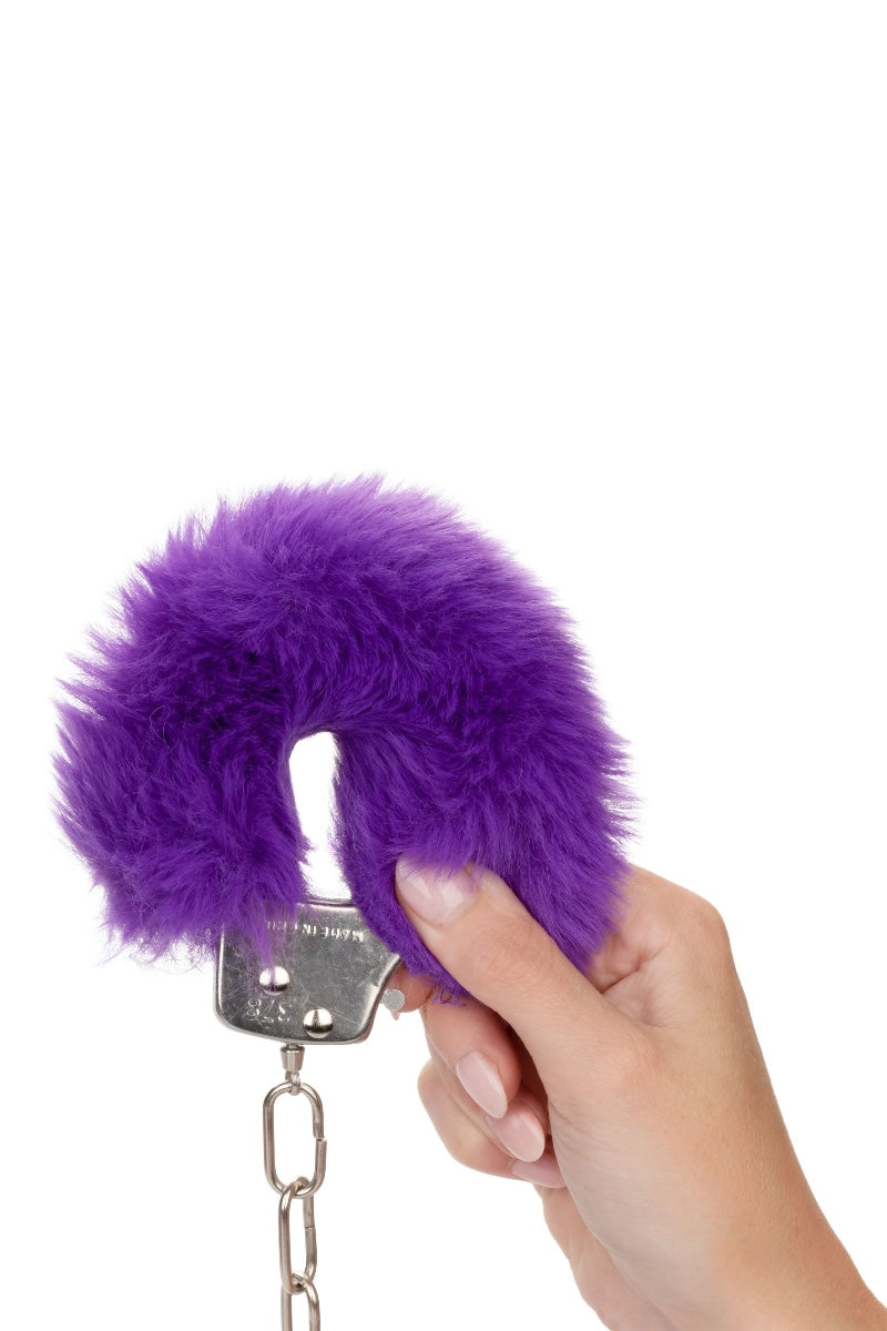 Purple fluffy handcuff held by a hand on a white background