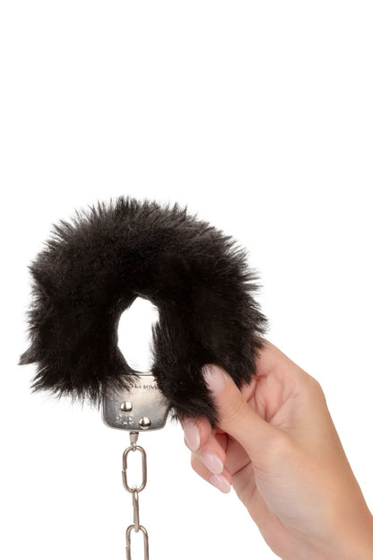 Hand holding a black furry handcuff attached to a chain on a white background