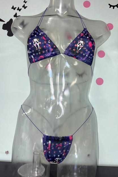 A two-piece bikini set displayed on a transparent mannequin torso. The bikini features a dark purple base with a repeating pattern of white and pink Ghostfaces, along with small white and pink stars.