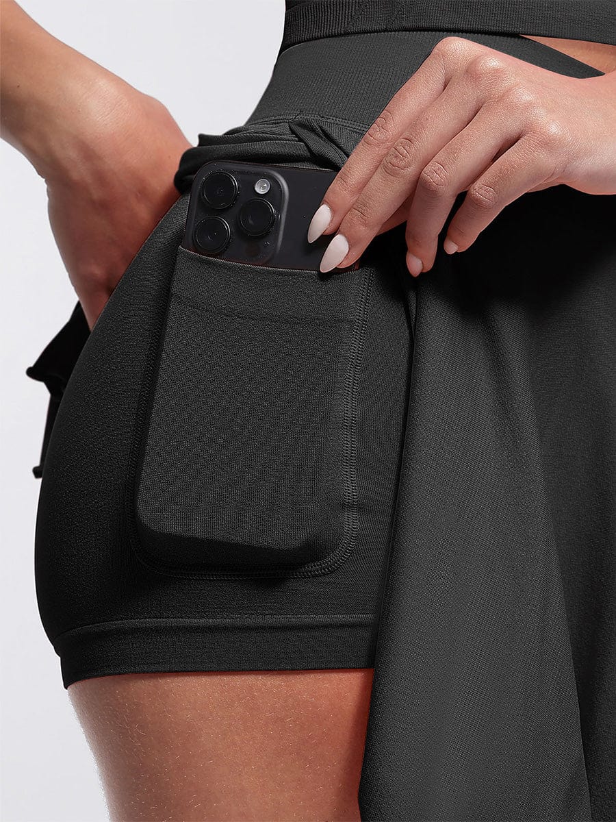 Person wearing black shorts with a pocket holding a phone on a light gray background