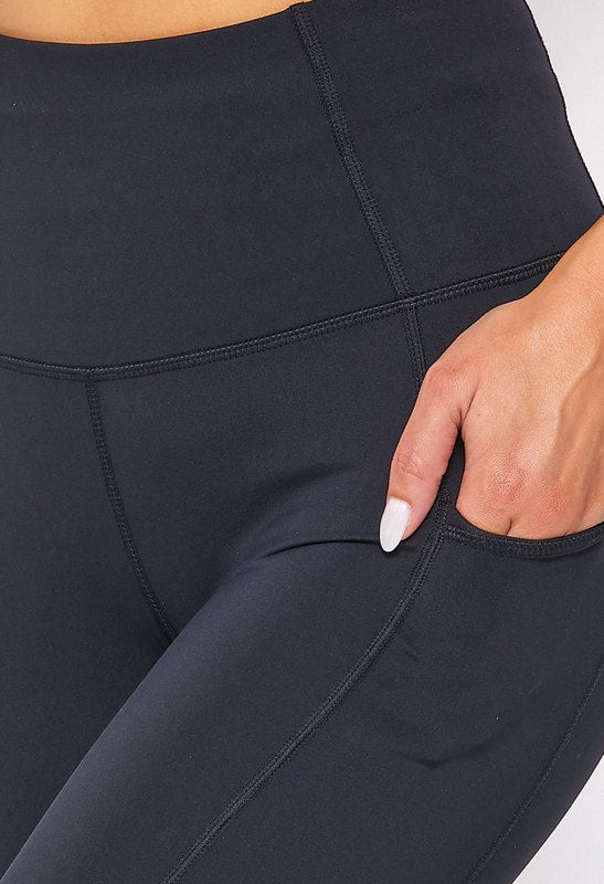 Close-up of black leggings with a hand in the pocket on a white background